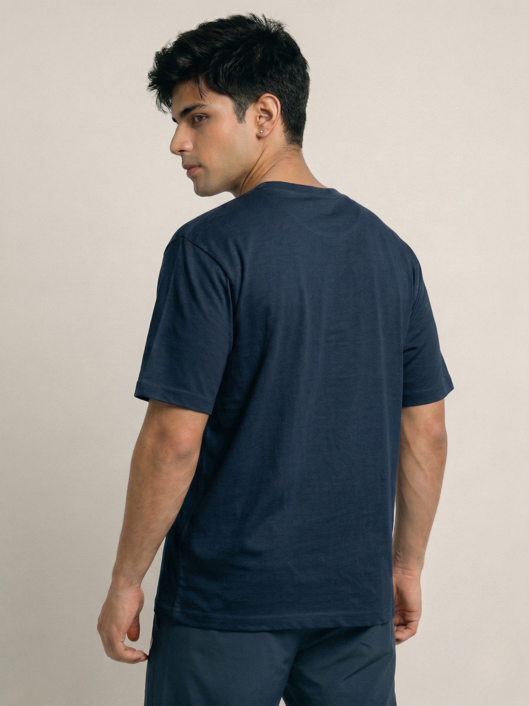 Man wearing a navy blue t-shirt and pants against a beige background